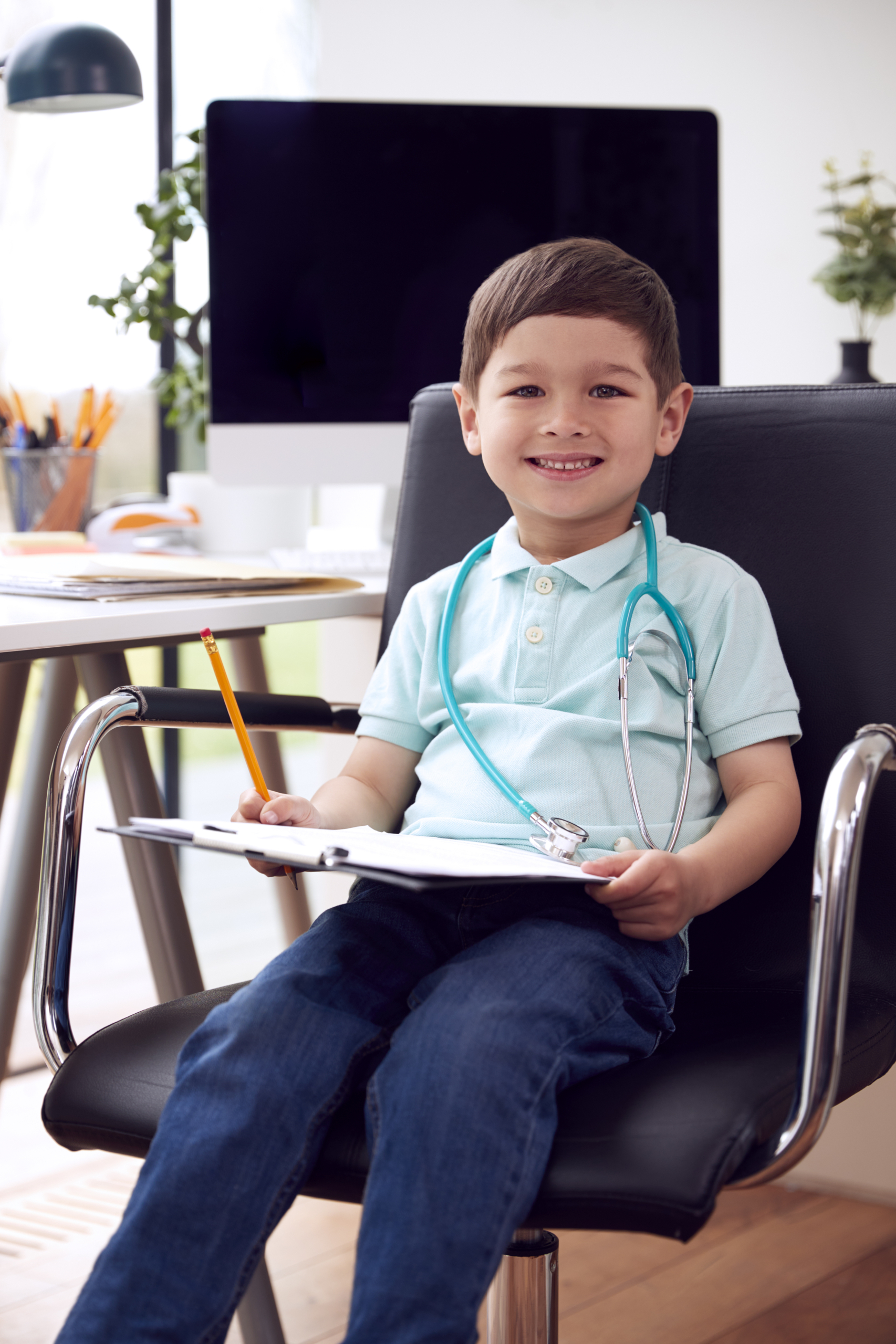 Portrait Of Smiling Young Boy Sitting In Chair In Office Pretending To Be Doctor