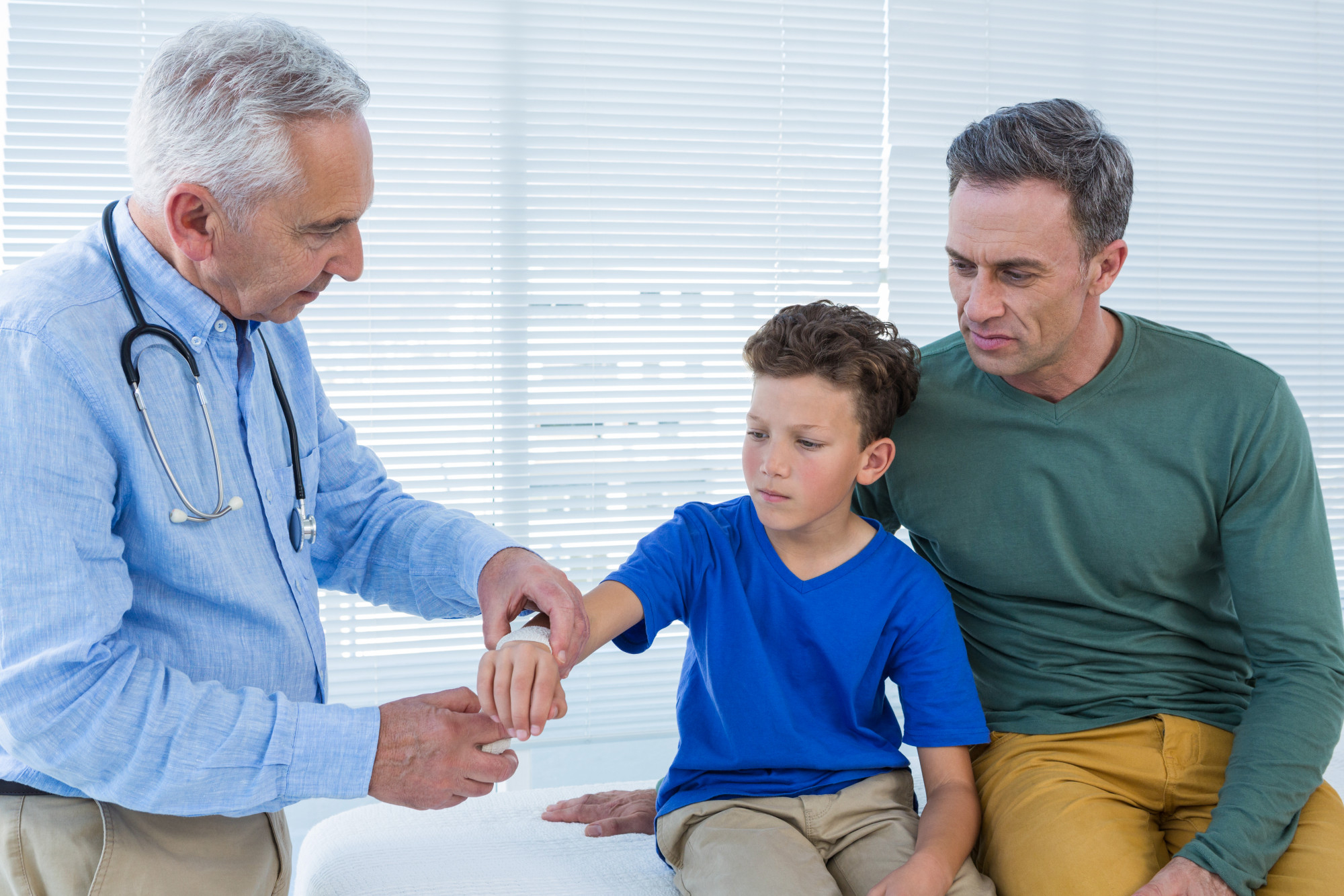 Arzt untersucht den Arm eines Jungen, während der Vater aufmerksam daneben sitzt – medizinische Nachsorge bei Circumvision